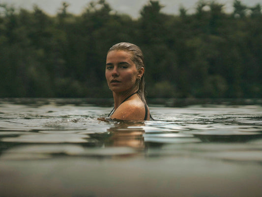 Woman with wet hair in a lake up to her shoulders, forest behind