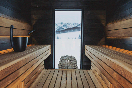 Dark wooden sauna with slatted benches, a stone heater and a window onto snowy mountains